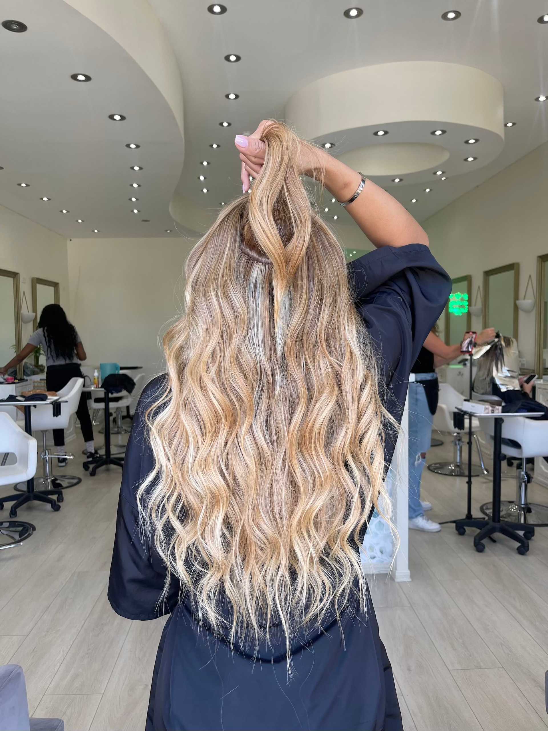 Woman in salon with long wavy blonde hair, holding a section up.