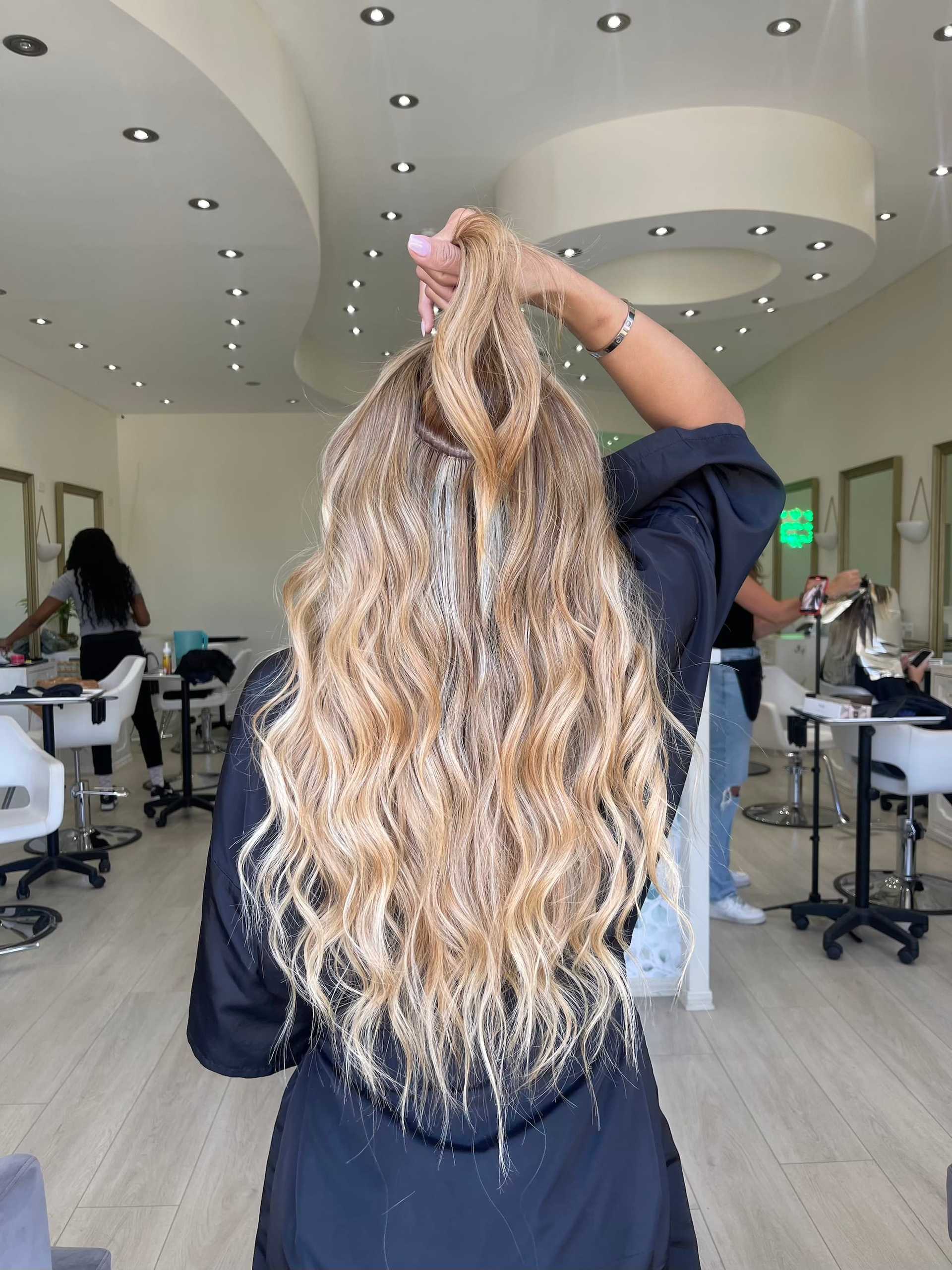 Woman in salon with long wavy blonde hair, holding a section up.