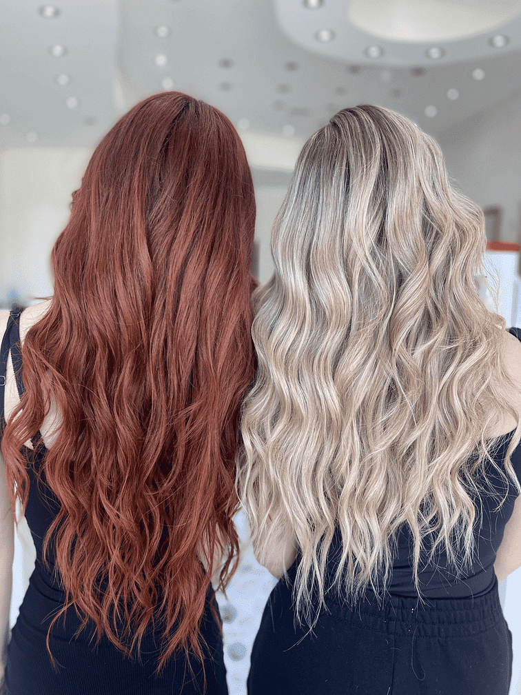 Two women with long, wavy red and blonde hair in black outfits, seen from the back.