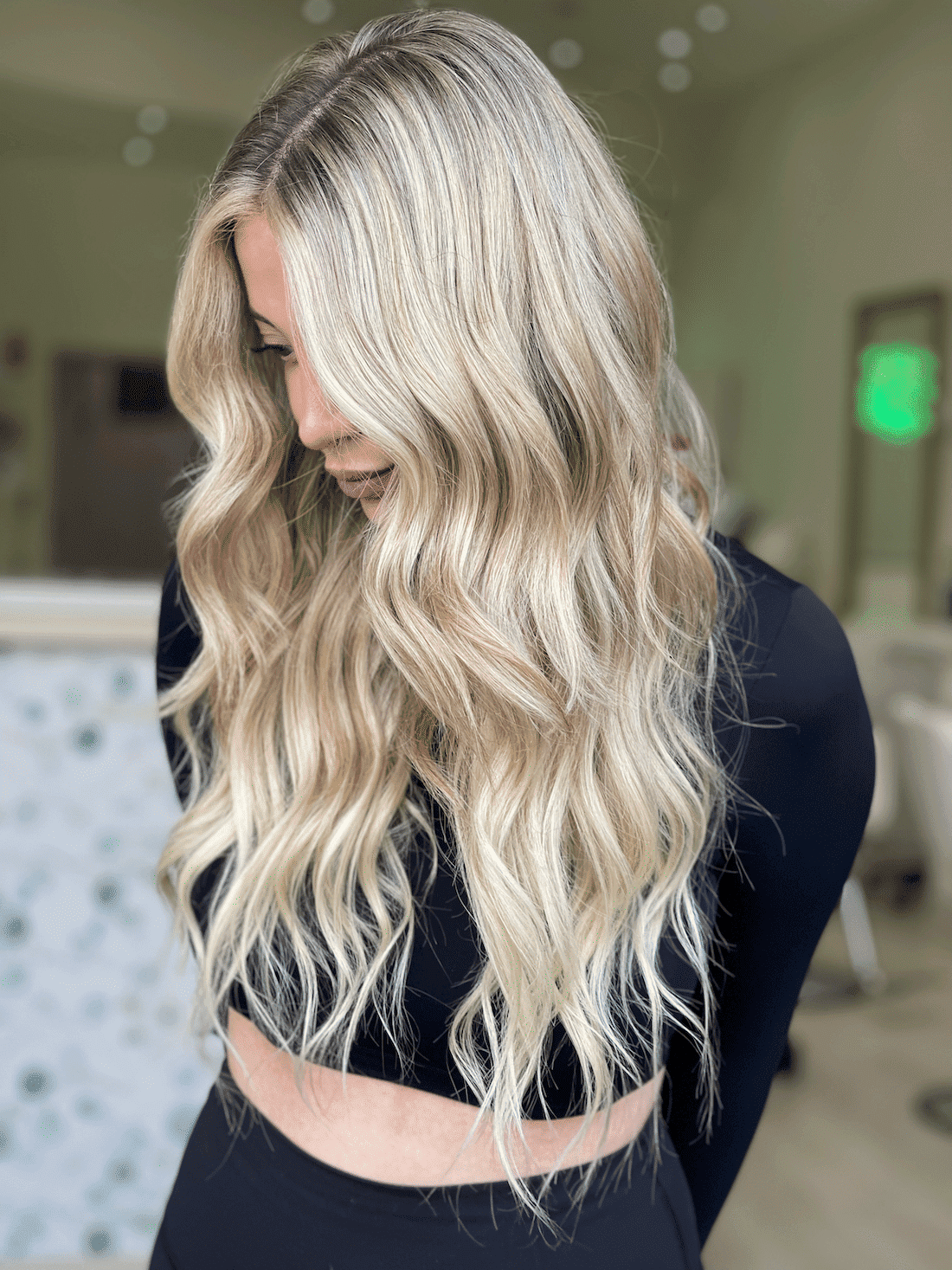 Long wavy blonde hair on a person wearing a black outfit, in a salon setting.